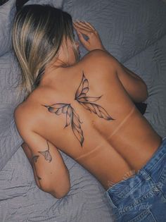 a woman laying on top of a bed with tattoos on her back and arms behind her head