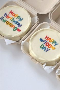 three decorated birthday cakes in plastic containers on a white table with the words happy birthday written on them