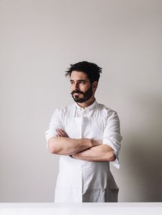 a man with his arms crossed standing in front of a white table and looking at the camera