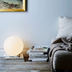 a lamp sitting on top of a wooden floor next to a pile of books and a couch