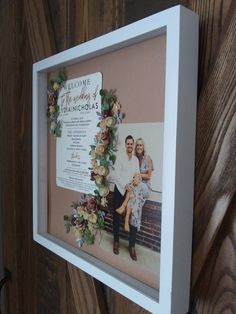 a white framed photo with flowers hanging on a wooden wall