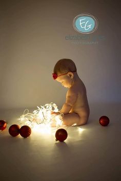 a baby is sitting on the floor playing with some christmas balls and lights in front of him