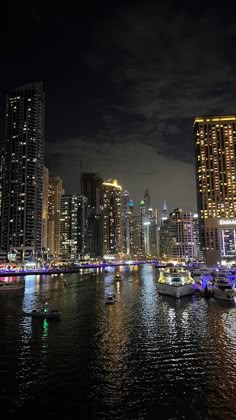 the city skyline is lit up at night with boats in the water and buildings on both sides