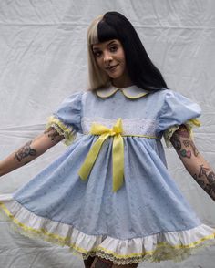 a woman dressed in a blue dress with yellow ribbon around her waist and tattoos on her arms