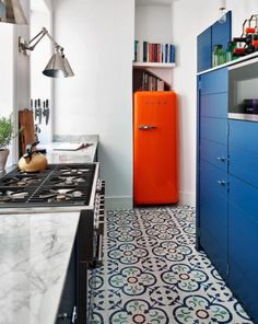 a kitchen with blue cabinets and an orange refrigerator in the center, next to a white tiled floor