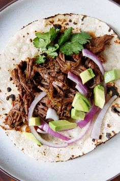 a taco with meat, onions, and avocado on a white plate