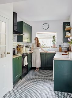 a woman standing in a kitchen with green cabinets