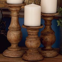 three white candles sitting on top of wooden posts in front of a window sill