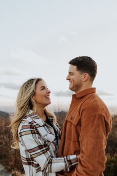 a man and woman standing close to each other in front of the camera, looking into one another's eyes