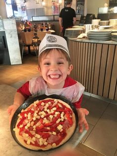 a little boy holding up a pizza in front of him