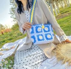 a woman sitting on the ground holding a blue and yellow purse with daisies in it