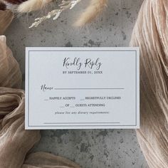 a wedding response card on a table with feathers and fabric in the background, as seen from above