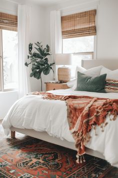 a bed with white sheets and pillows in a bedroom next to a potted plant