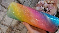 a hand holding a rainbow colored case with glitter on the outside and inside, in front of a brick wall