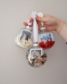 three ornaments hanging from the ceiling with pictures and flowers in them, one being held by a woman's hand