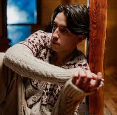 a young man leaning against a wall with his hand on the door handle and looking at something