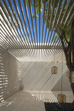 an outdoor room with white walls and wooden slats on the ceiling is lit by sunlight