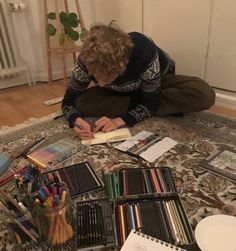 a woman is sitting on the floor with many books and pencils in front of her