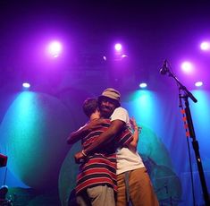 two men hugging each other on stage with purple lights behind them and microphones in the background