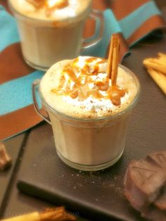 two cups filled with hot chocolate and topped with whipped cream, cinnamon sticks and caramel