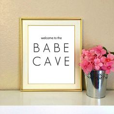 there is a vase with pink flowers next to a framed sign that says babe cave