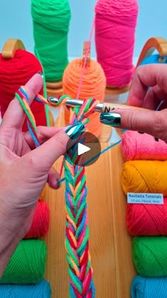 two hands are working with yarn on a wooden table next to colorful balls of yarn