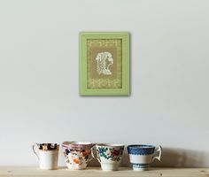 three cups are lined up on a shelf in front of a framed picture with a woman's head