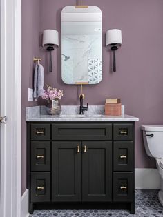 a bathroom with purple walls and white fixtures on the vanity, along with a gold framed mirror