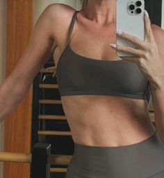 a woman taking a selfie with her cell phone in front of her face and wearing a gray sports bra top