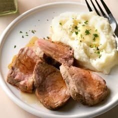 a white plate topped with meat and mashed potatoes next to a knife and fork