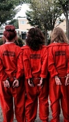 five women in red jumpsuits are walking down the street with their hands on their hips