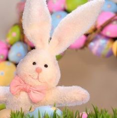 an easter bunny sitting in the grass with eggs and flowers behind it, on a table