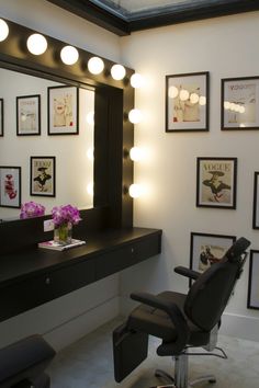 a chair in front of a mirror with lights on it and pictures hanging on the wall