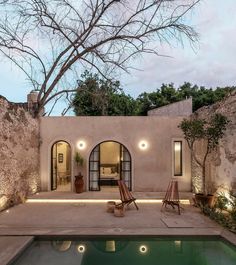 an outdoor swimming pool surrounded by stone walls and trees at dusk with the lights on