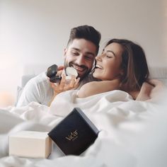 a man and woman laying in bed with their eyes closed, one is holding a small object