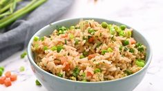 a bowl filled with rice and vegetables on top of a white table next to asparagus