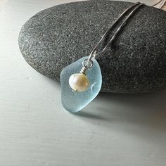 a blue sea glass pendant with a pearl on it sitting on top of a rock