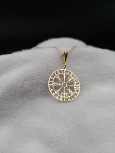 a gold plated necklace with a compass on it's back end, sitting on top of a white blanket