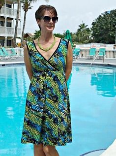 a woman standing in front of a swimming pool wearing sunglasses and a colorful dress with green accents