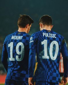 two soccer players in blue uniforms standing next to each other with their hands on their hips