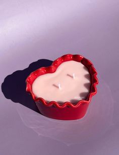 a candle in a red bowl on a white surface with the shadow of a heart