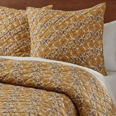 a bed with yellow and brown comforters on it's headboard next to a night stand