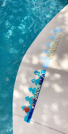 a surfboard that is sitting on the side of a body of water in front of a swimming pool