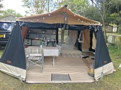 a tent set up in the grass with tables and chairs under it, next to a van