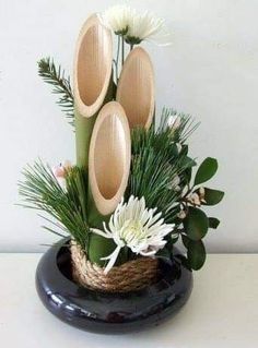 an arrangement of flowers and greenery in a black vase on a white table top