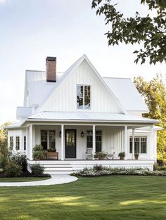 a white house with a black door and windows on the front porch is surrounded by lush green grass