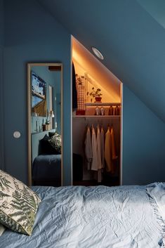 an attic bedroom with blue walls and white linens on the bed, closet doors open to reveal clothes