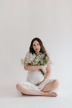 a woman is sitting on the floor with flowers in her hand and she is wearing a white dress