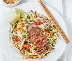 a white plate topped with meat and veggies next to chopsticks