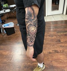 a man with a tattoo on his arm is standing in front of a clock and flowers